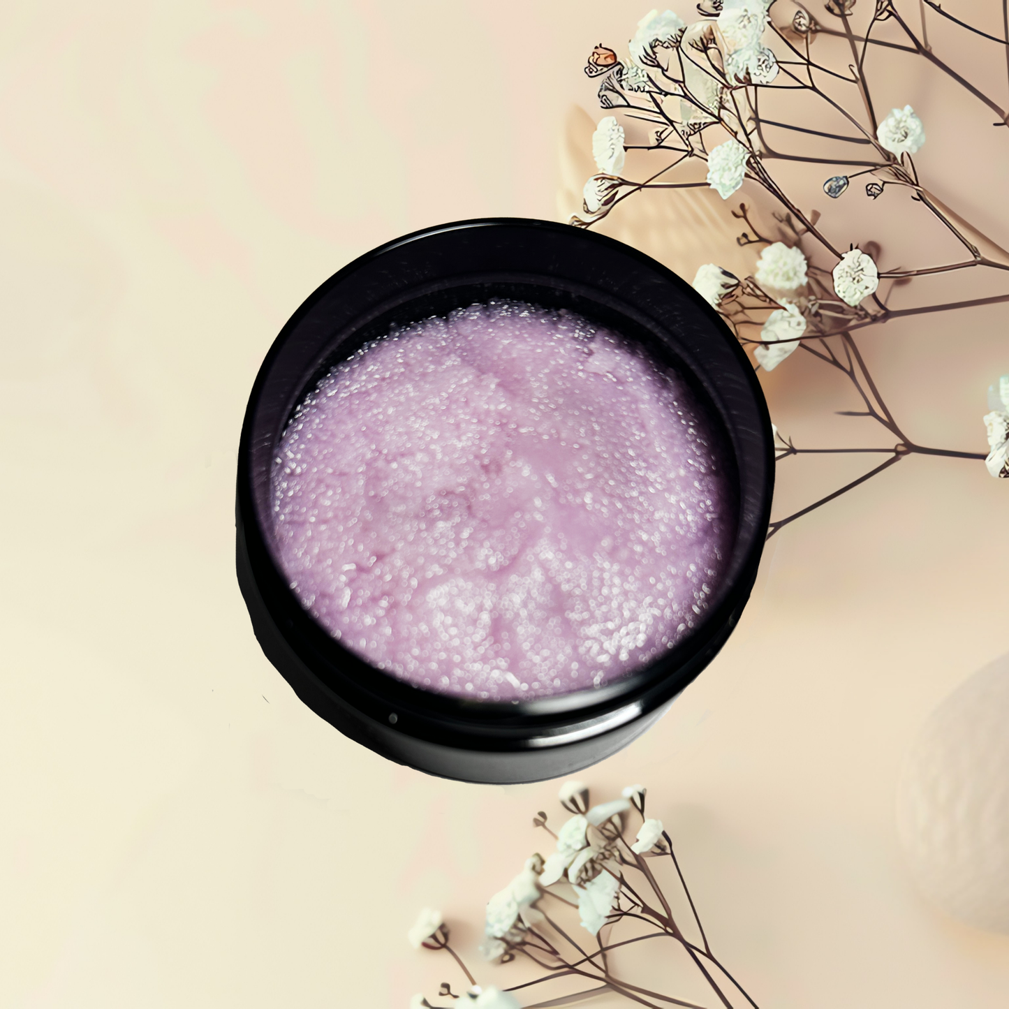 Black bowl with purple sugar scrub on a beige background with white flowers