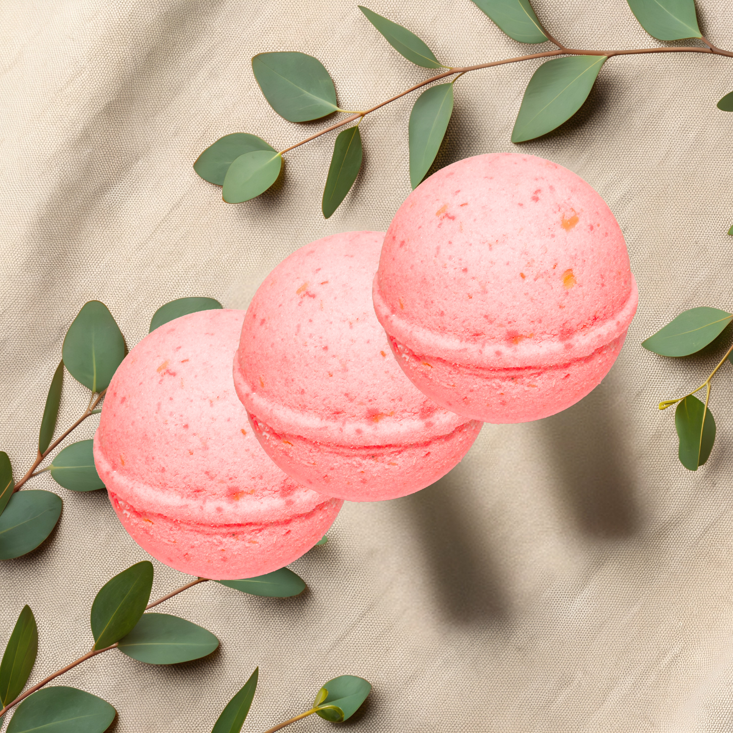 Three pink bath bombs with green leaves on a beige fabric background