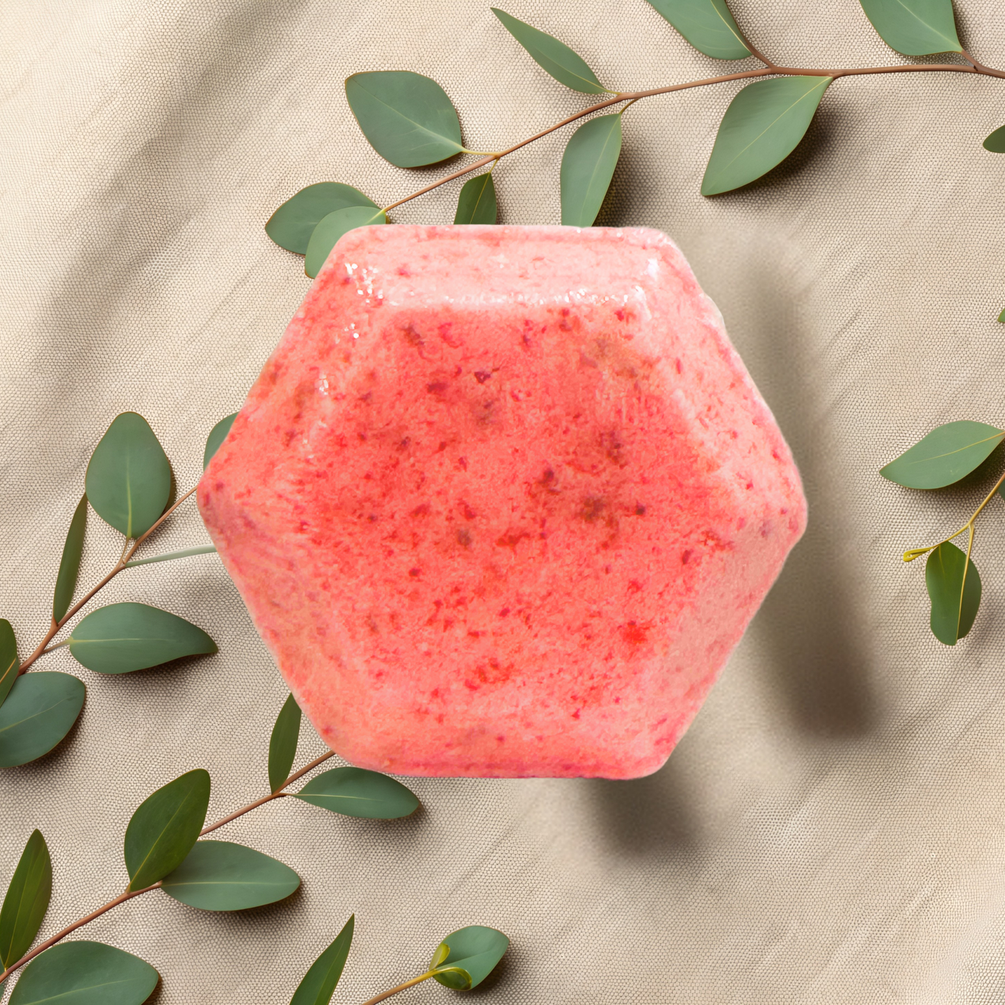 Hexagonal pink shower bomb with green leaves on a beige fabric background