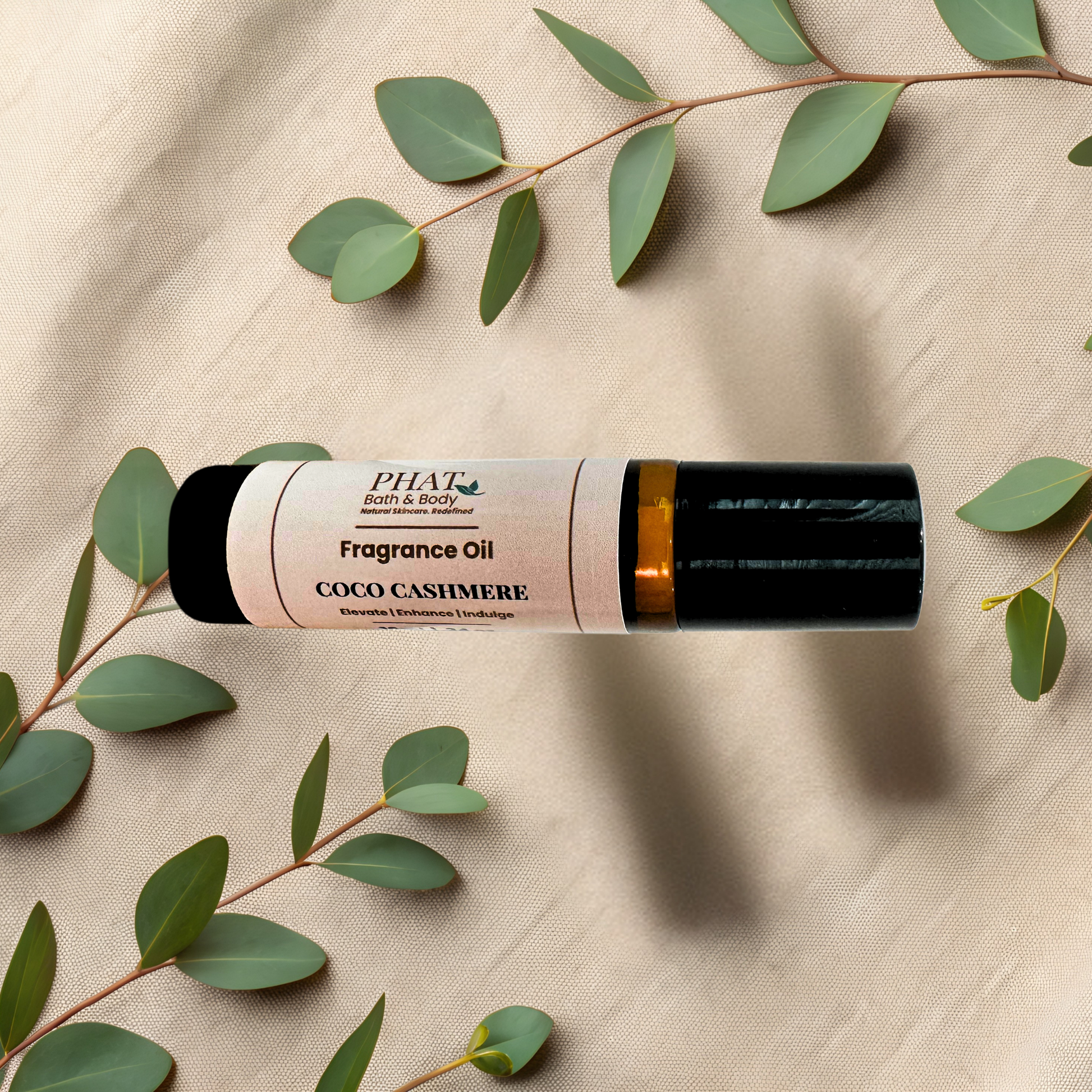 A bottle of Fragrance Oil in the Coco Cashmere scent, styled on a beige textured fabric background with green eucalyptus leaves.
