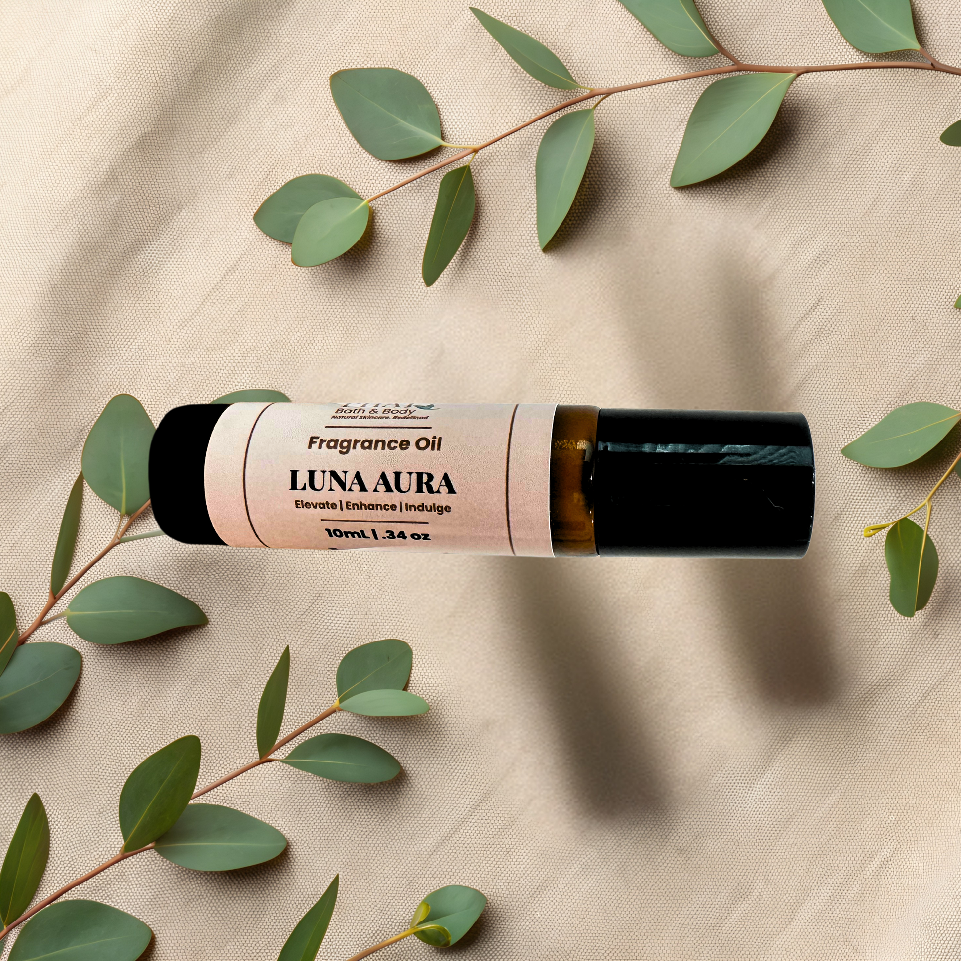 A 10ml roll-on bottle of Luna Aura Fragrance Oil, featuring a black cap, styled on a beige textured fabric background with green eucalyptus leaves.
