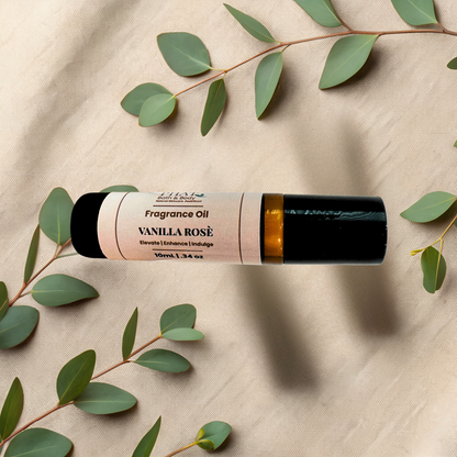 A roll-on bottle of Vanilla Rosé fragrance oil, styled on a beige fabric background with green eucalyptus leaves.
