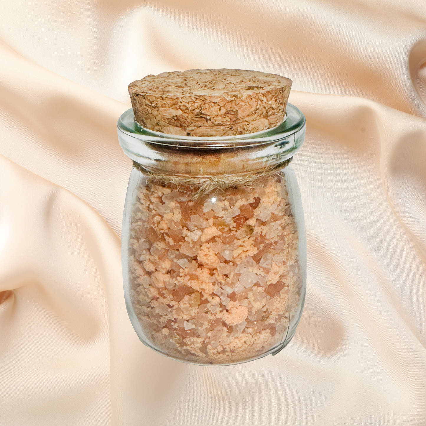Glass jar with cork lid containing a brown bath salts on a beige fabric background