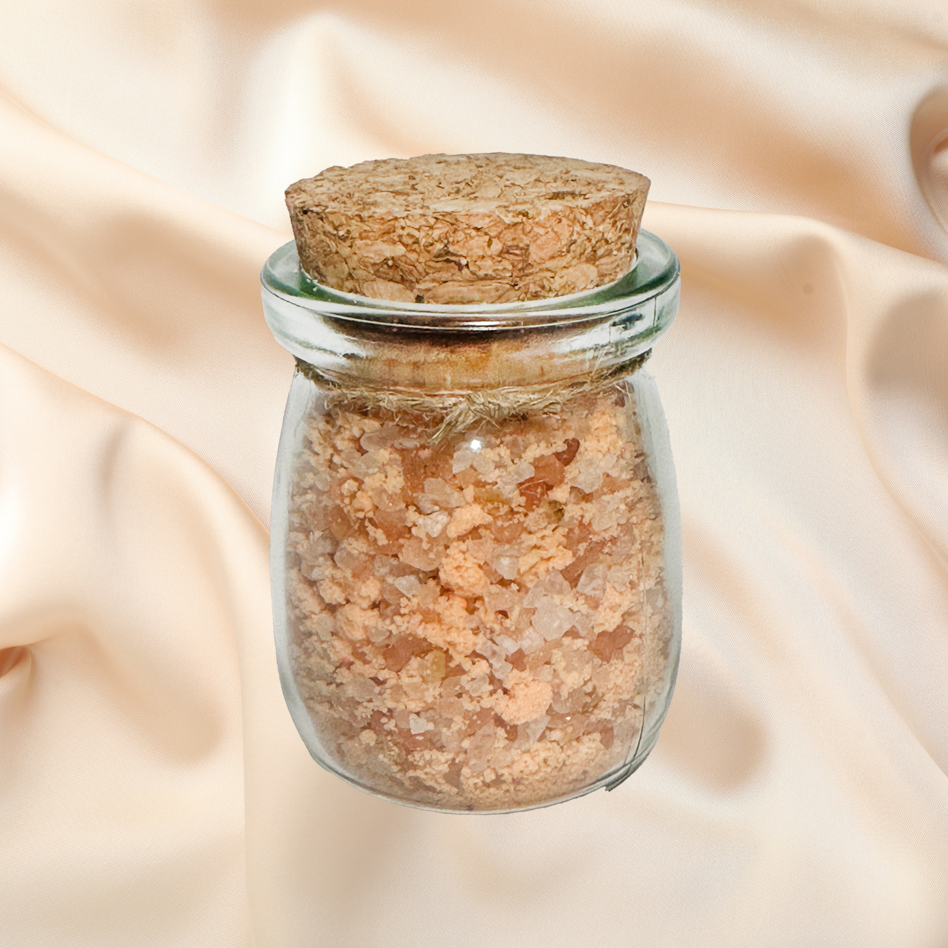 Glass jar with cork lid containing a brown bath salts on a beige fabric background