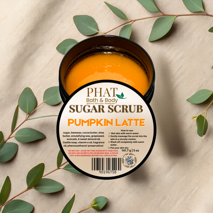 Jar of pumpkin latte sugar scrub with Phat Bath & Body branding on a beige fabric background with green leaves.