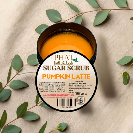 Jar of pumpkin latte sugar scrub with Phat Bath & Body branding on a beige fabric background with green leaves.