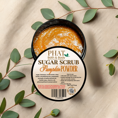 Pumpkin powder sugar scrub in a container with a 'Phat Bath & Body' label on a beige fabric background with green leaves.