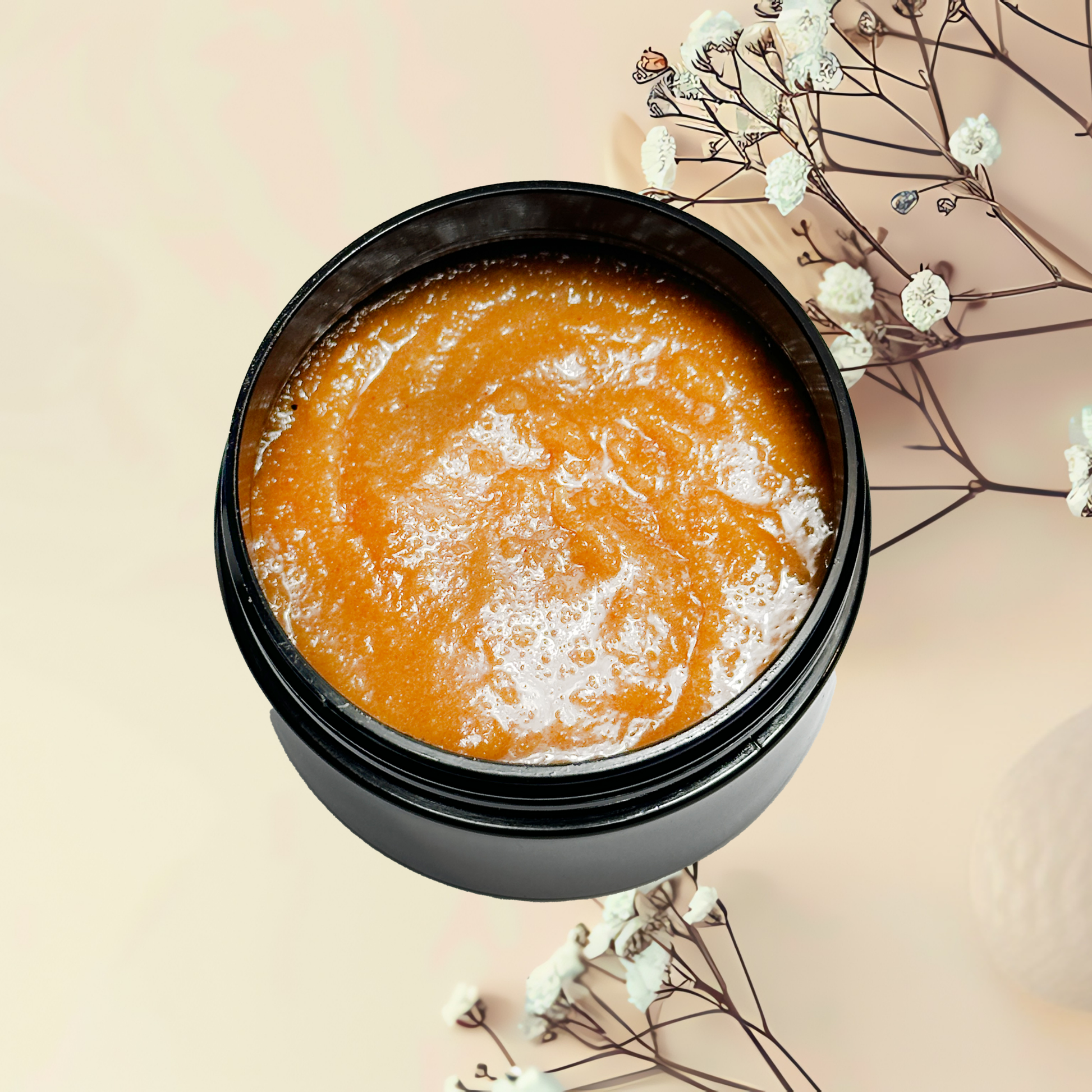Open jar of orange scrub with white flowers on a beige background
