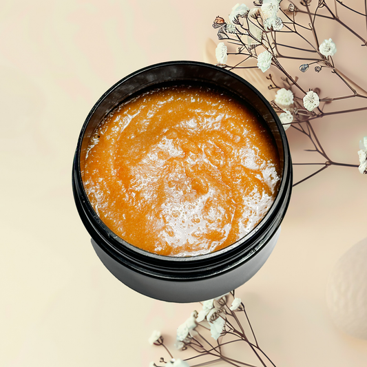 Open jar of orange scrub with white flowers on a beige background