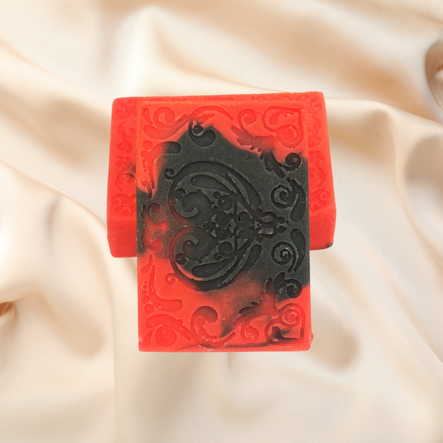 Red and black decorative soap with intricate patterns on a beige fabric background