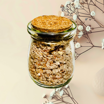 Glass jar with cork lid containing bath salts, surrounded by delicate flowers on a light background