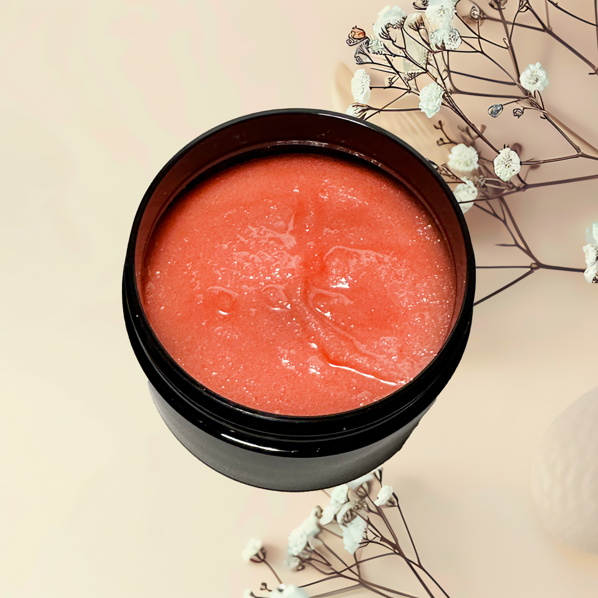Black container with pinkish-red scrub on a beige background with white flowers.