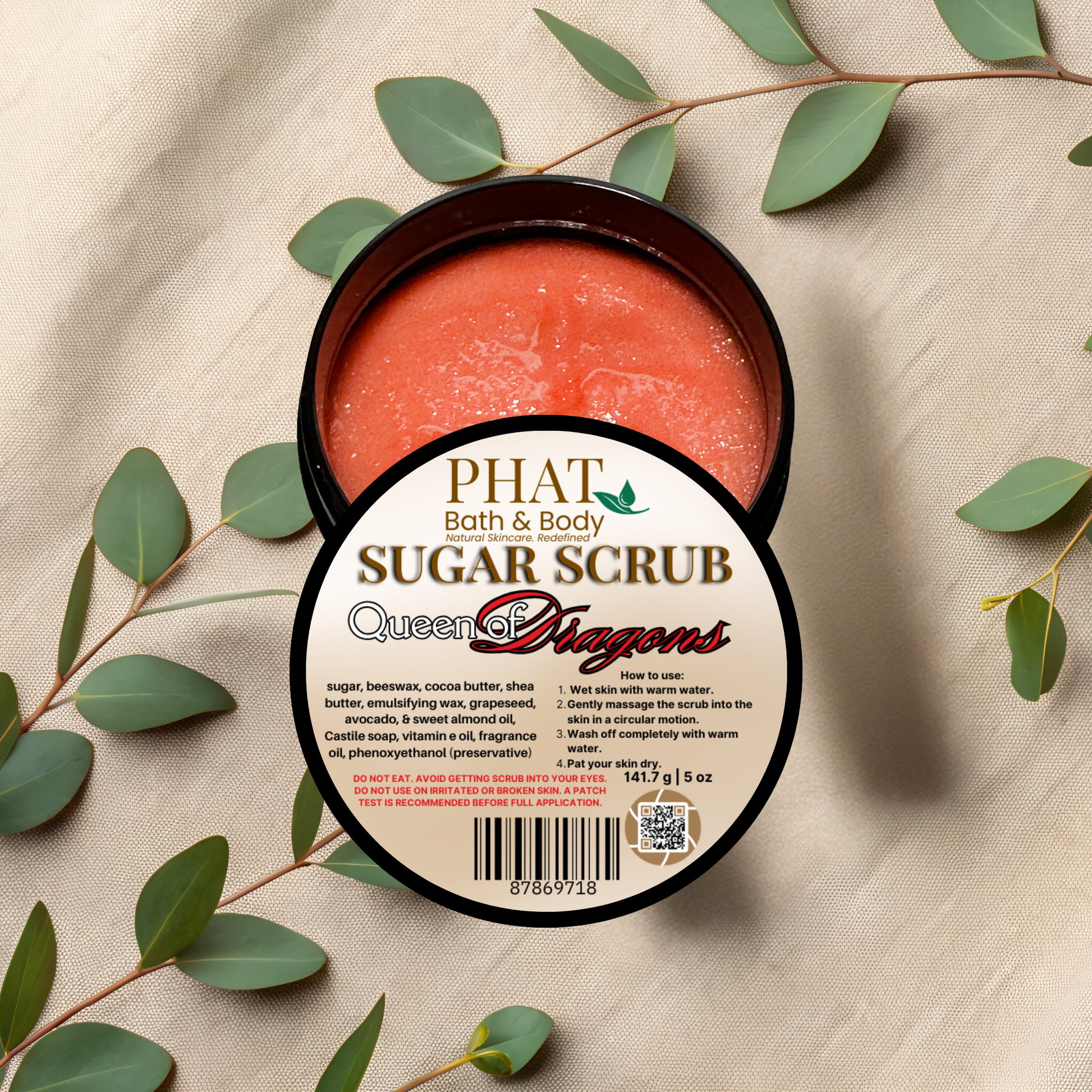 Jar of sugar scrub with a label on a beige fabric background with green leaves.