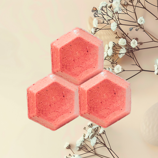 Three pink hexagonal shower bombs with white flowers on a beige background