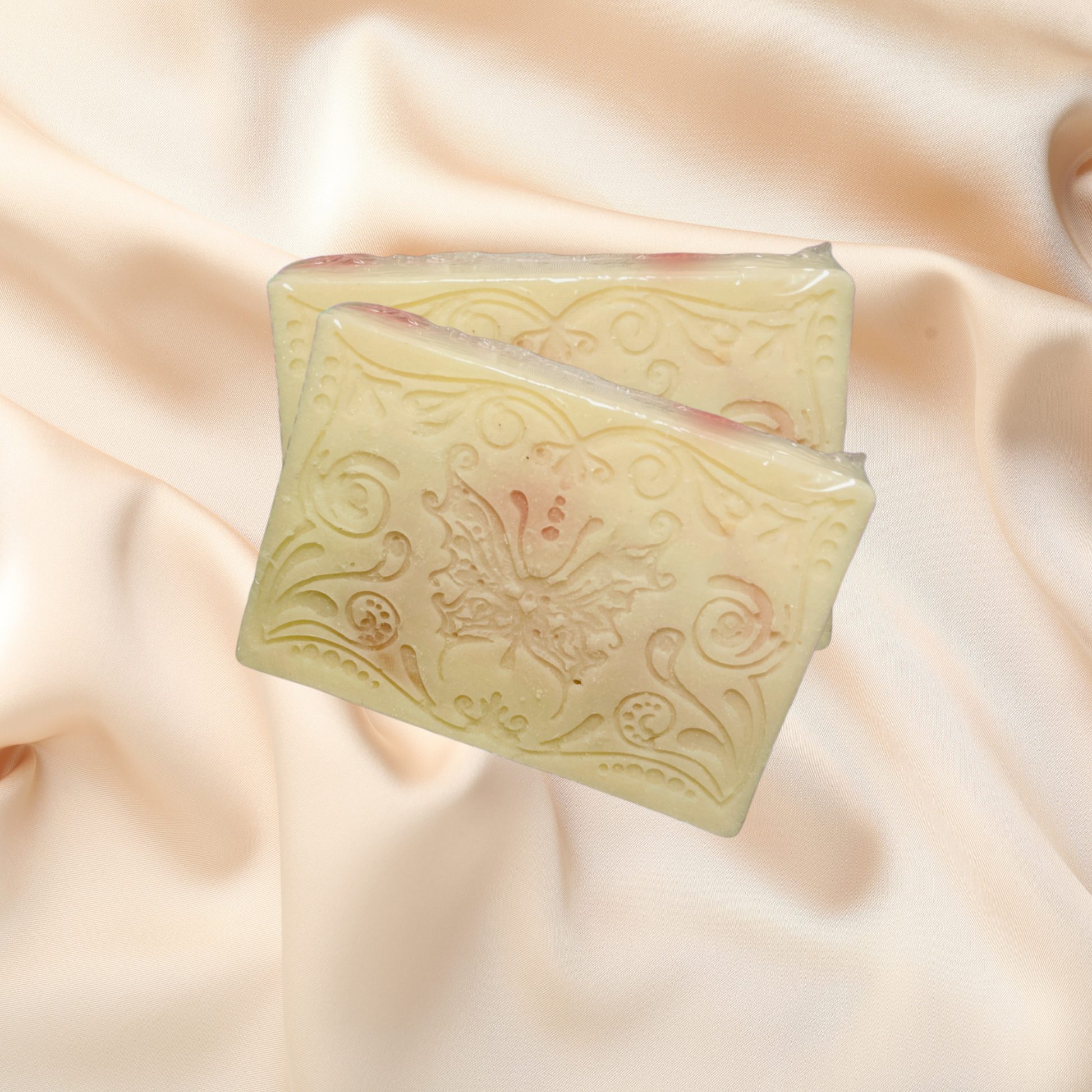 Two rectangular bars of soap with embossed designs on a soft, light pink fabric background