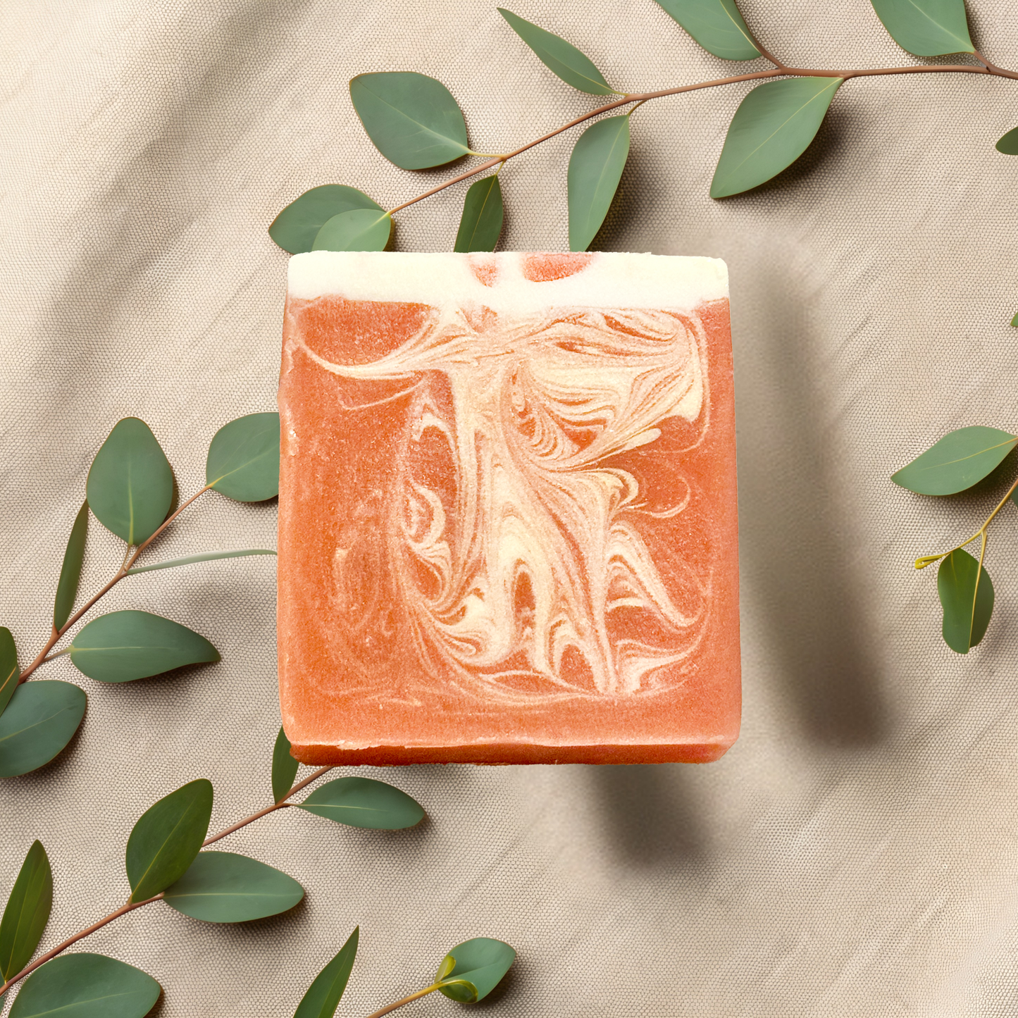 Marbled soap bar with green leaves on a beige fabric background