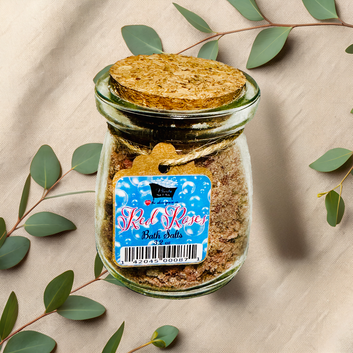 Jar of bath salts with a label on a beige fabric background with green leaves.