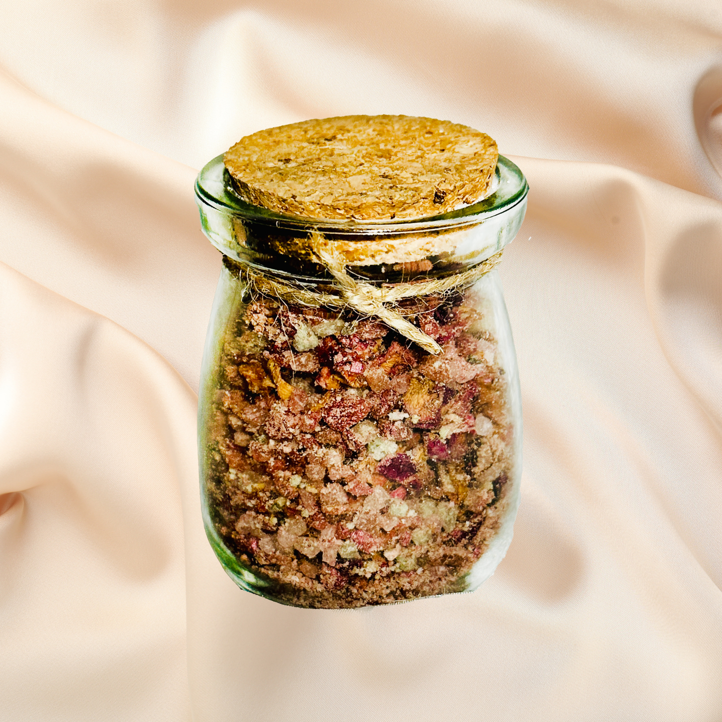 Glass jar with cork lid containing a mix of bath salts on a soft beige fabric background