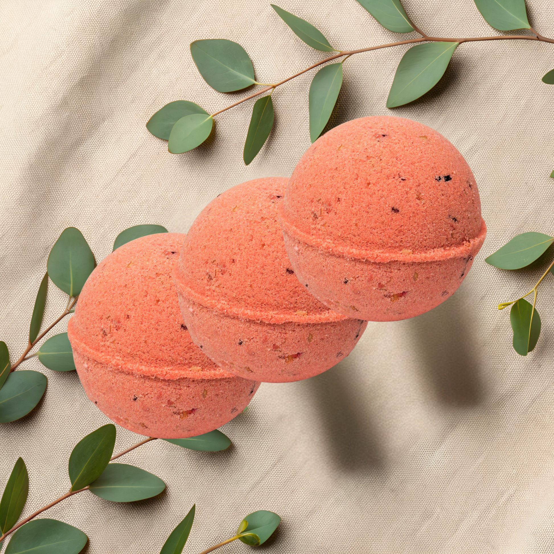 Three red bath bombs with green leaves on a beige fabric background
