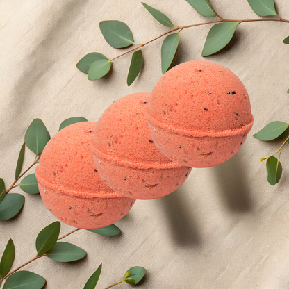 Three red bath bombs with green leaves on a beige fabric background