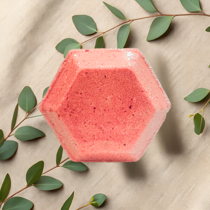 Hexagonal pink shower bomb on a beige fabric background with green leaves