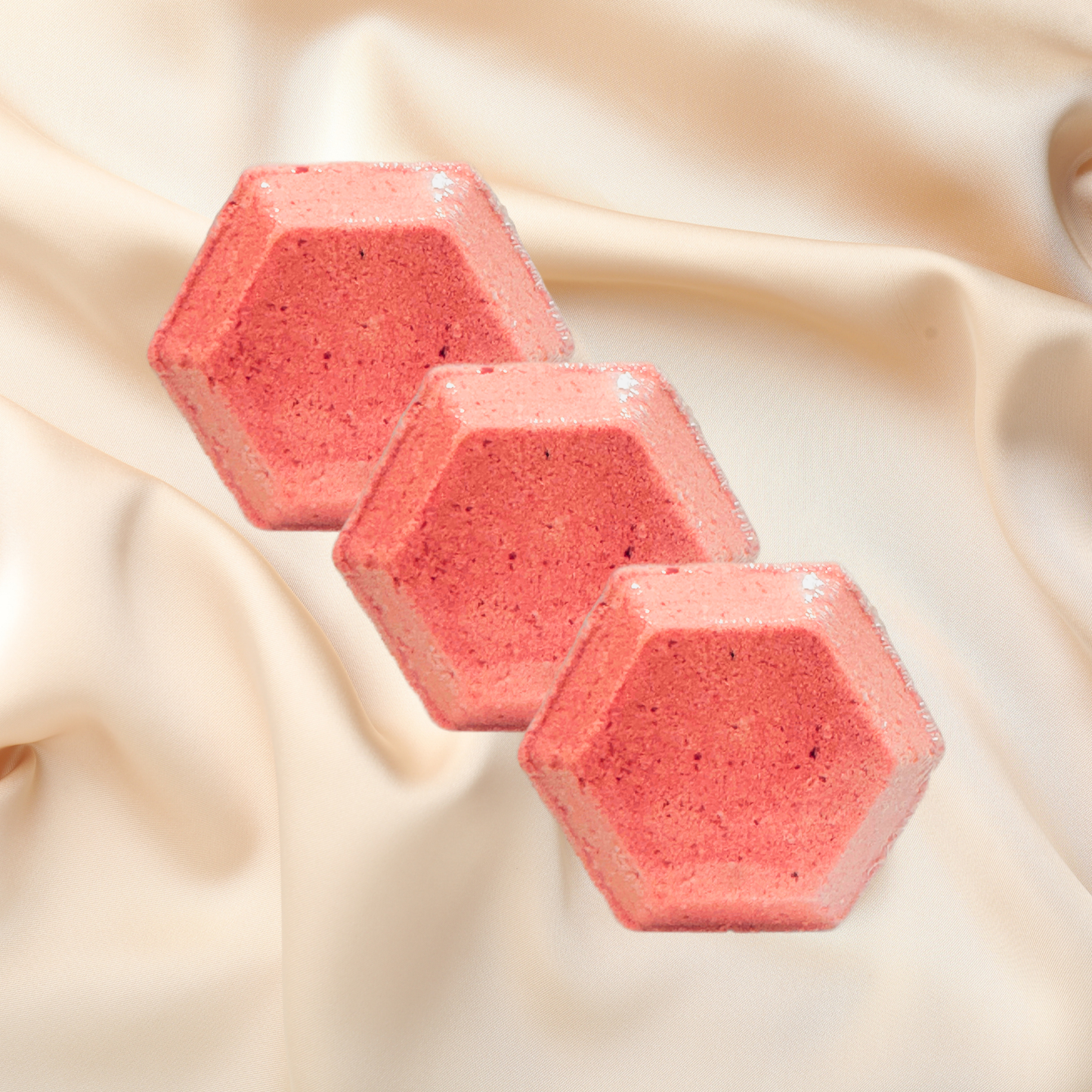 Three pink hexagonal shower bombs on a beige fabric background
