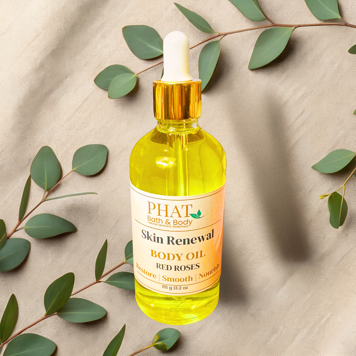 Bottle of PHAT Bath & Body Skin Renewal Body Oil with Red Roses scent on a beige fabric background with green leaves.