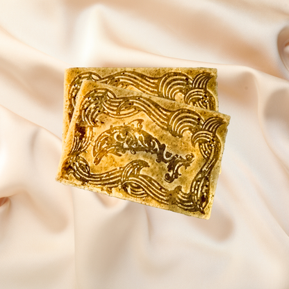 Two square soap bars with decorative patterns on a soft pink fabric background