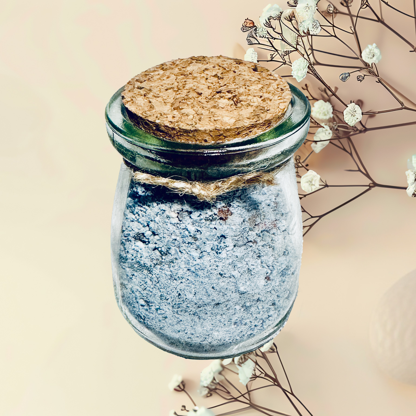 Glass jar with cork lid and blue bath salt, surrounded by dried flowers on a beige background