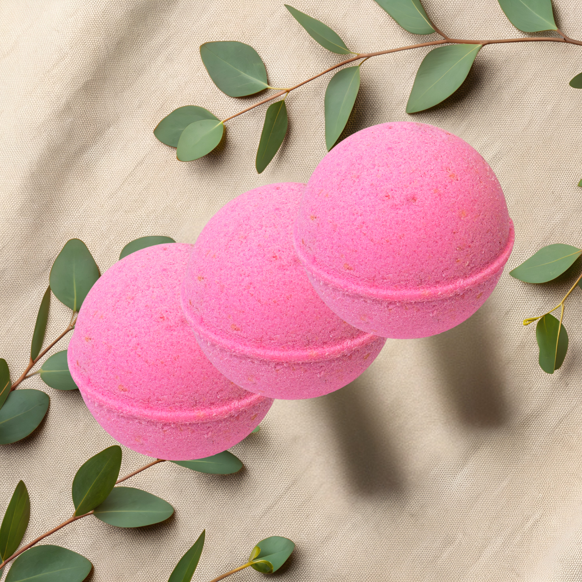 Three pink bath bombs with green leaves on a beige fabric background