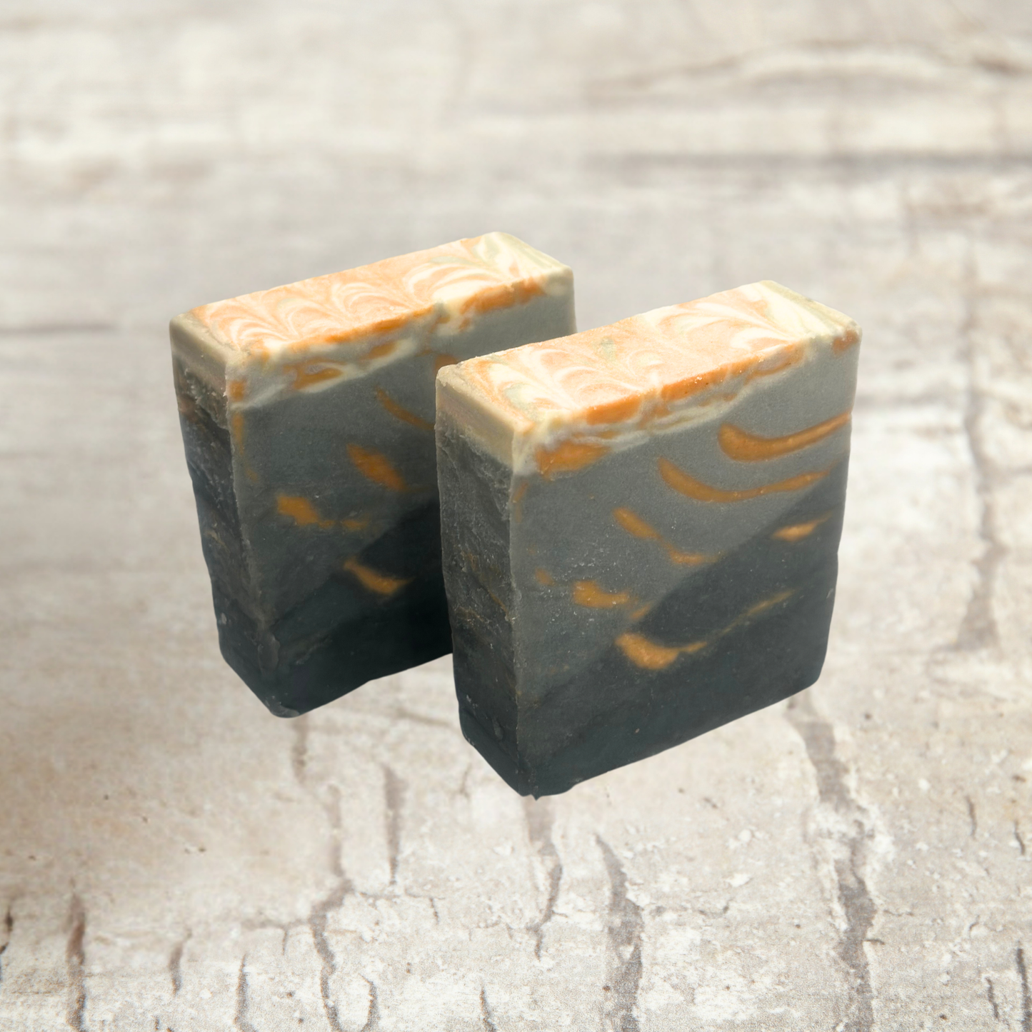 Two rectangular bars of soap with orange and black patterns on a textured surface