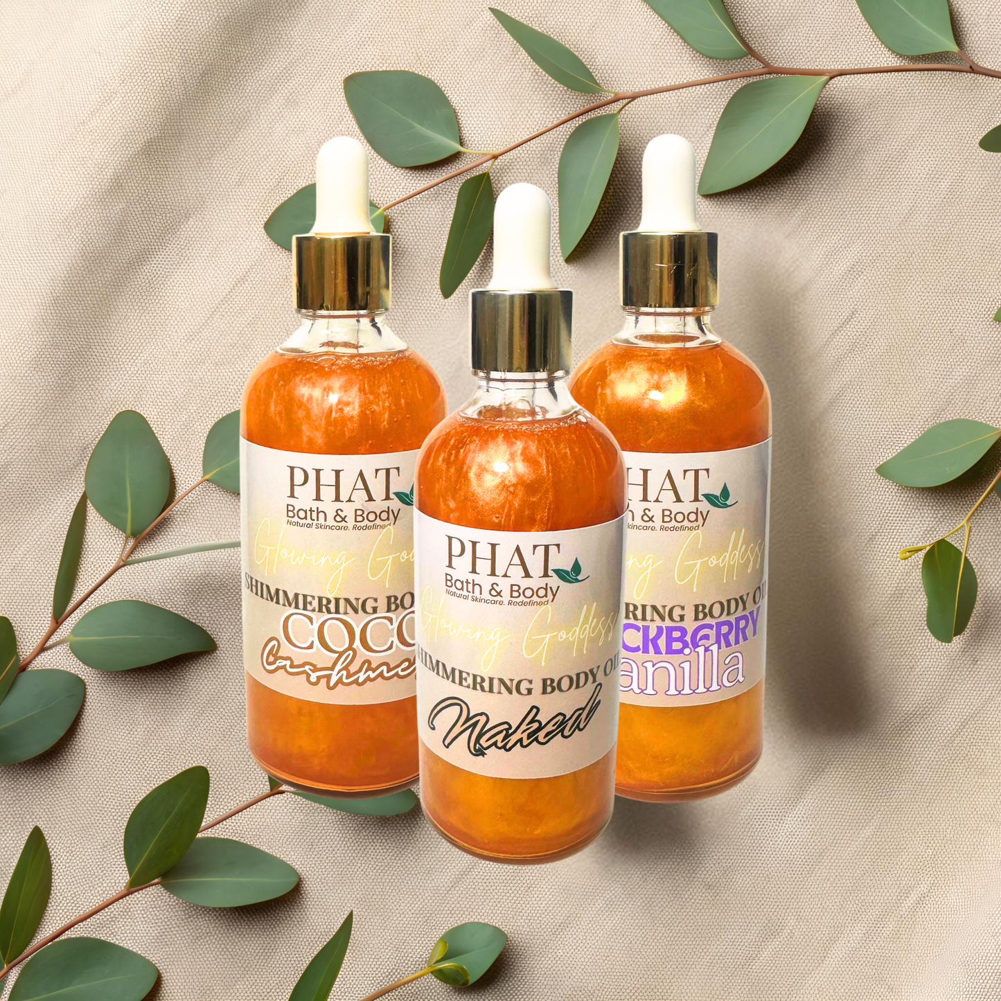 Three bottles of 'PHAT Bath & Body' shimmering body oils with green leaves on a beige fabric background.