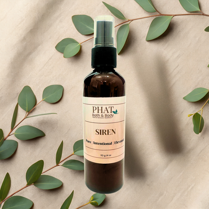 Bottle of 'Siren' by PHAT Bath & Body on a beige fabric background with green leaves.