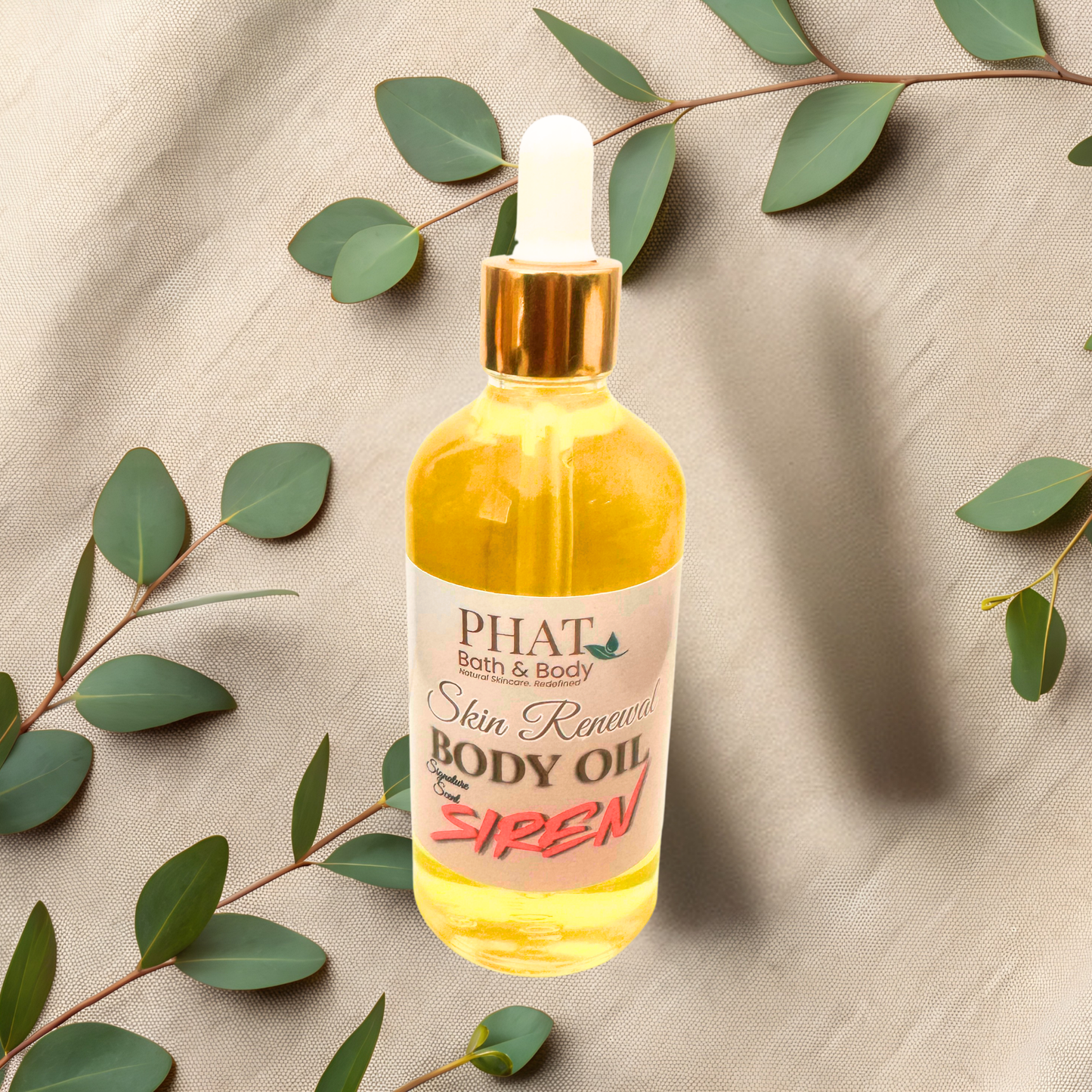 Bottle of 'PHAT Bath & Body' body oil with a dropper on a beige fabric background with green leaves.