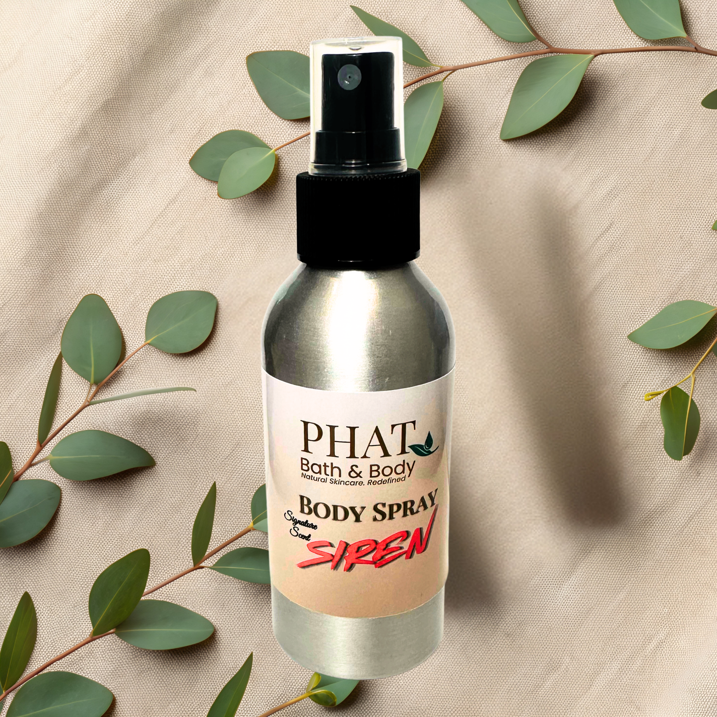Body spray bottle labeled 'PHAT Bath & Body' with 'Siren' on a beige fabric background with green leaves.