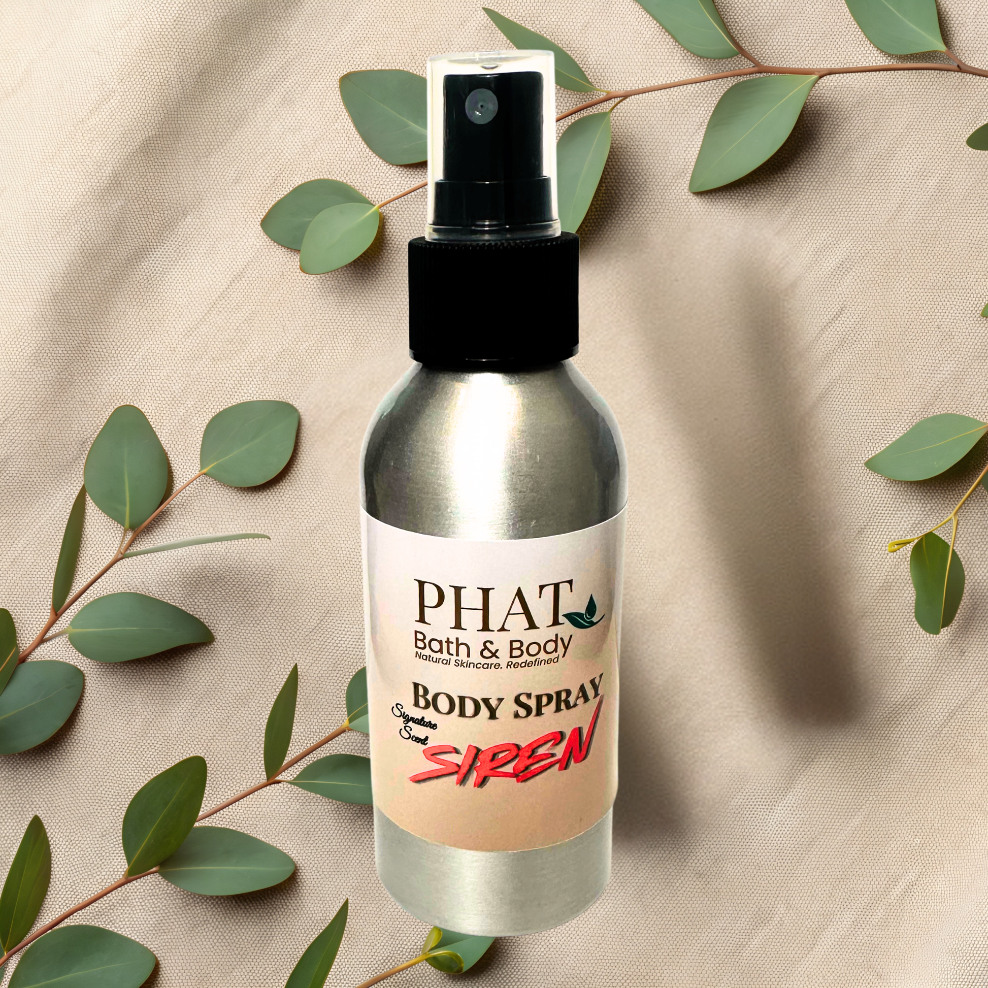 Body spray bottle labeled 'PHAT Bath & Body' with 'Siren' on a beige fabric background with green leaves.