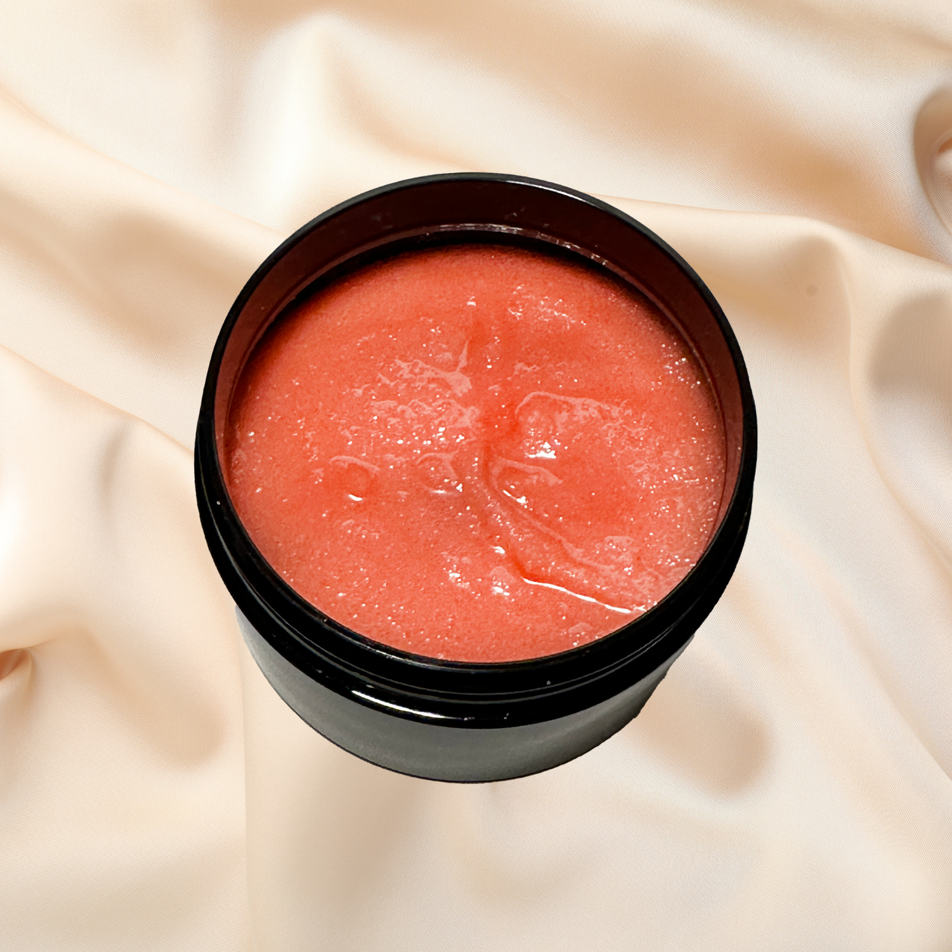 Black container with pinkish-red sugar scrub on a beige fabric background