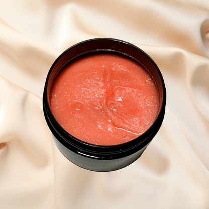 Black container with pinkish-red sugar scrub on a beige fabric background