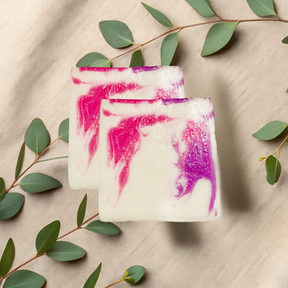 Two soap bars with pink and purple swirls on a beige fabric background with green leaves.