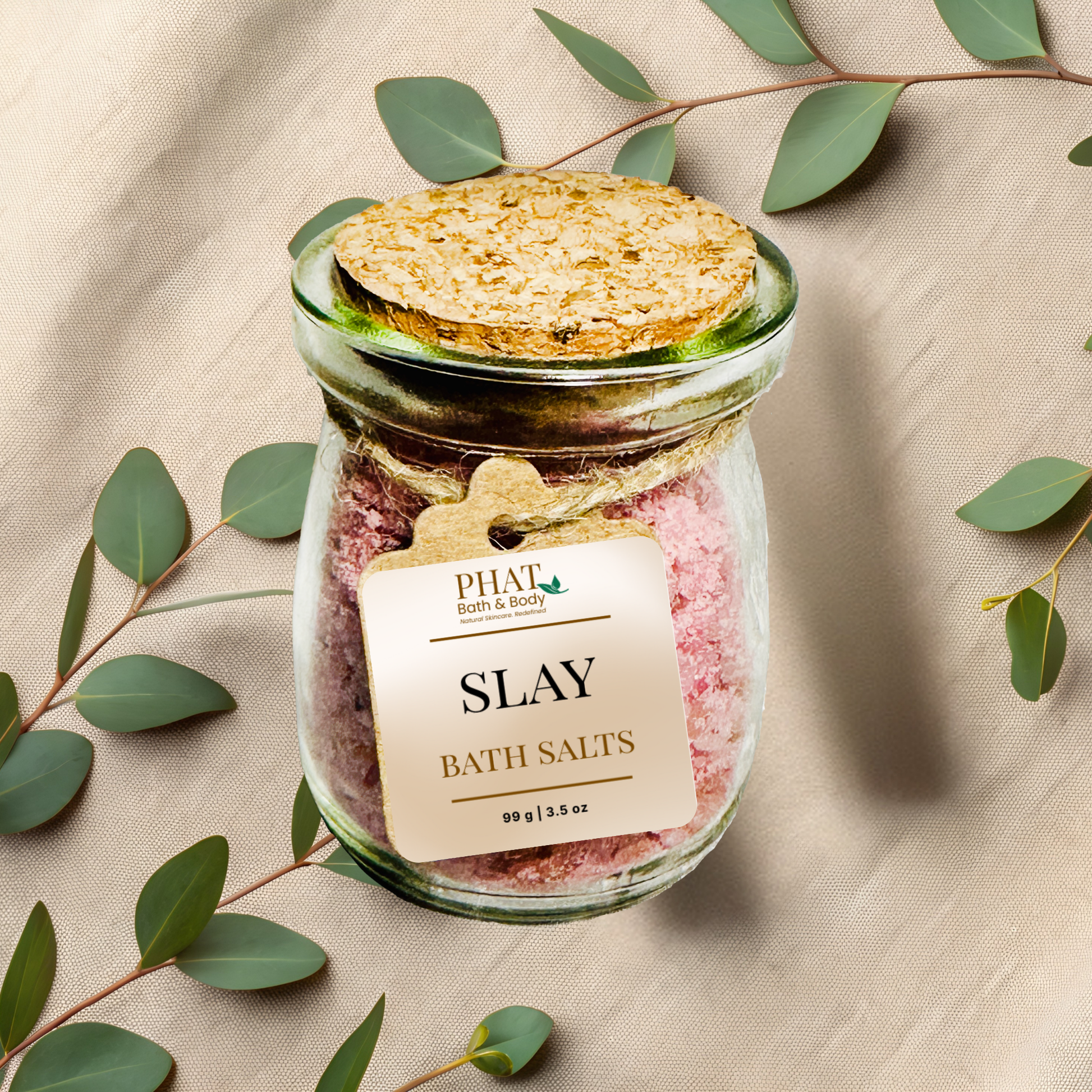 Jar of 'SLAY' bath salts on a beige fabric background with eucalyptus leaves.