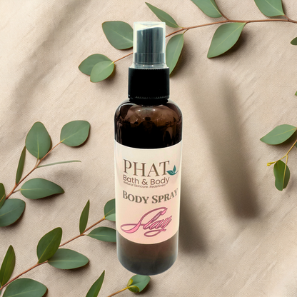 Body spray bottle with 'PHAT Bath & Body' label on a beige fabric background with green leaves.
