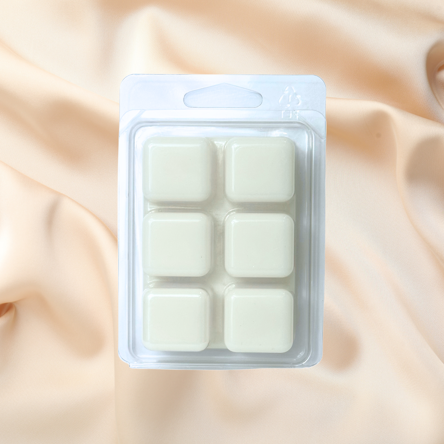 Pack of six white wax melts in a clear plastic packaging on a beige fabric background