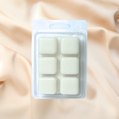 Pack of six white wax melts in a clear plastic packaging on a beige fabric background