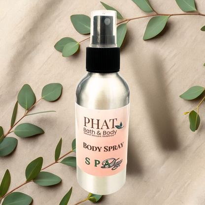 Body spray bottle with a pink label on a beige fabric background with green leaves.