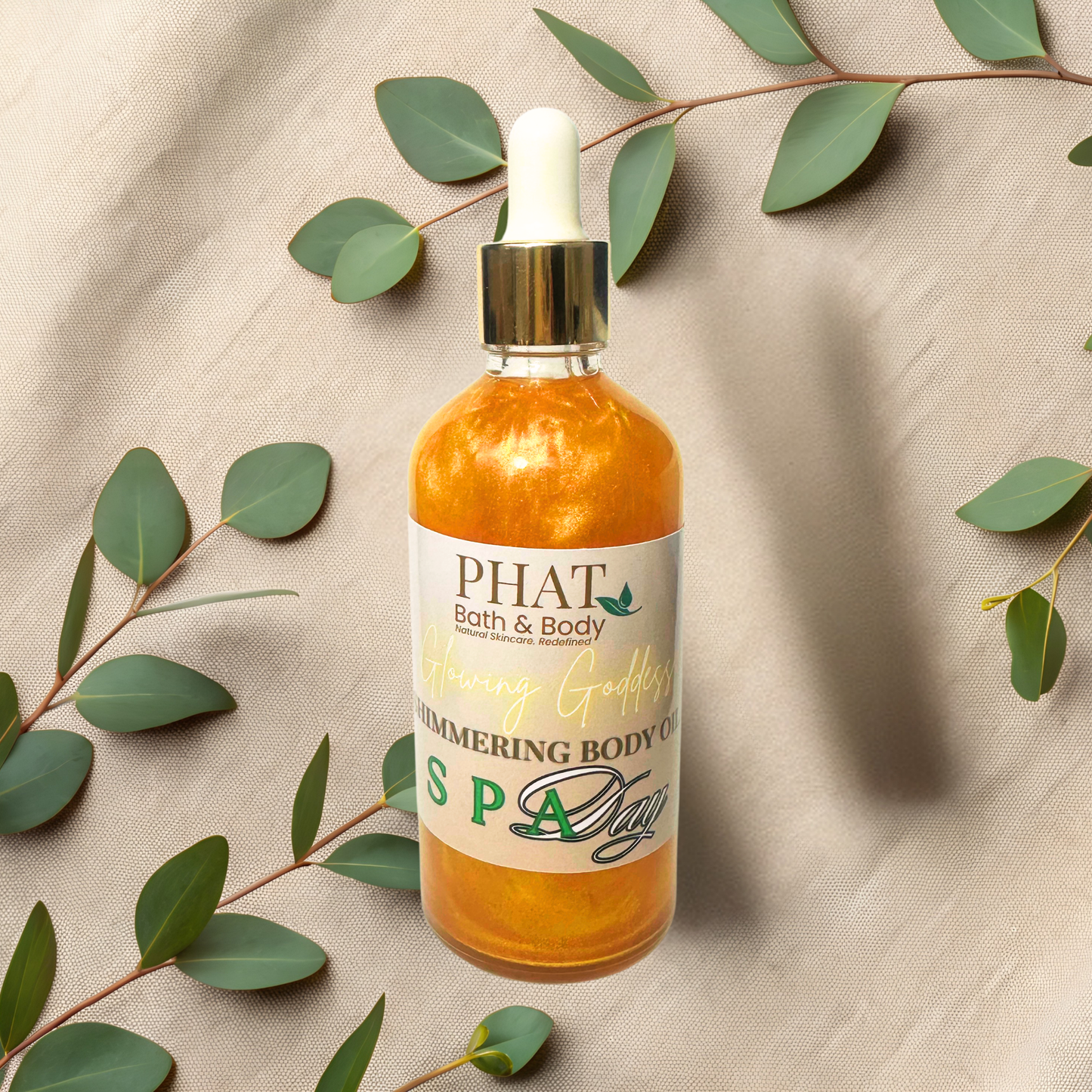 Bottle of 'PHAT Bath & Body' shimmering body oil with green leaves on a beige fabric background