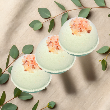 Three green bath bombs with pink salt on a beige fabric background with eucalyptus leaves.