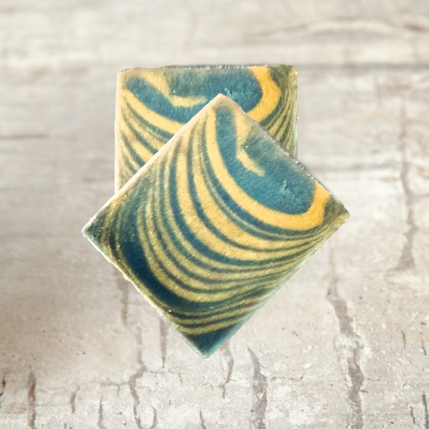 Two swirled green and yellow soap bars on a textured beige surface