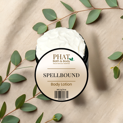Body lotion container labeled 'Spellbound' by PHAT Bath & Body on a beige fabric background with green leaves.