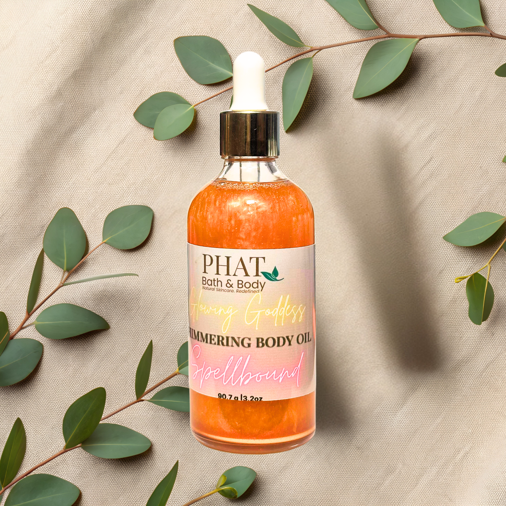 Bottle of PHAT Bath & Body shimmering body oil with green leaves on a beige fabric background