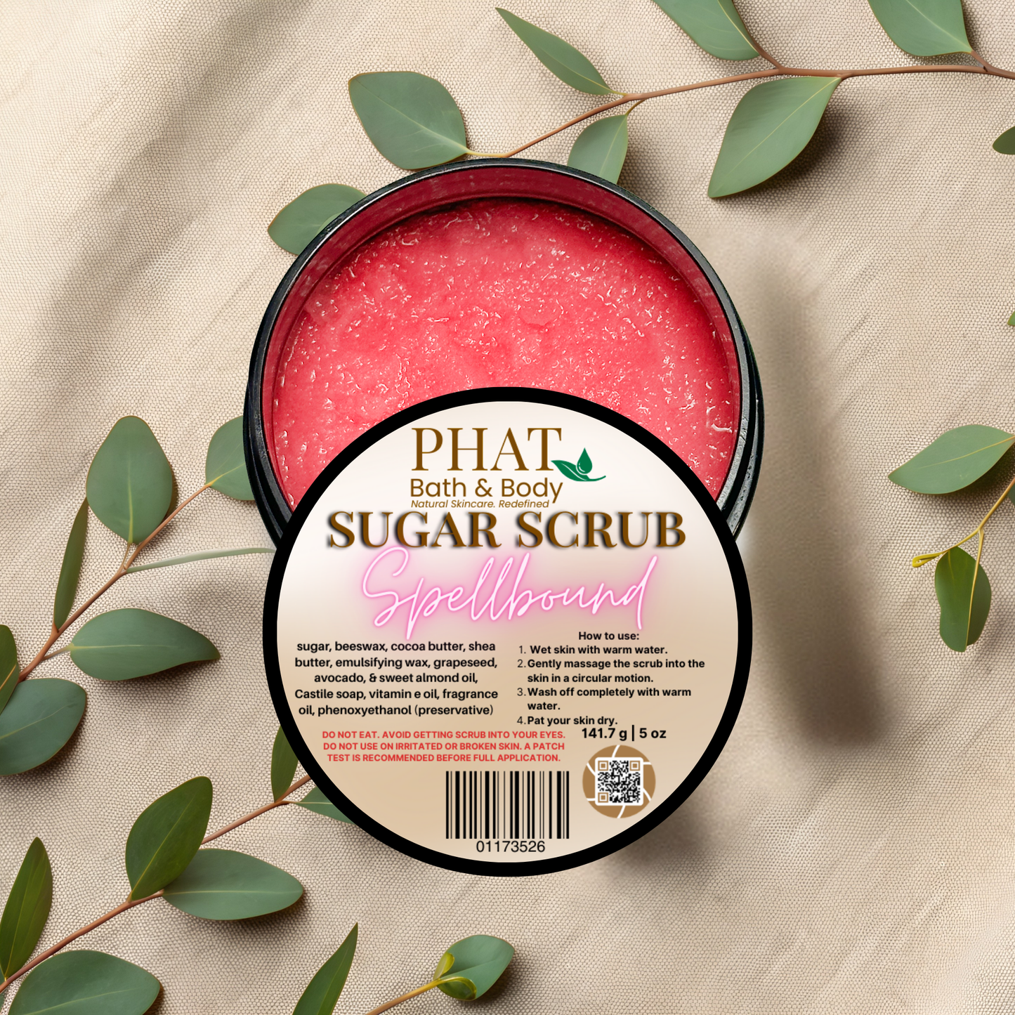 PHAT Bath & Body sugar scrub container with green leaves on a beige fabric background